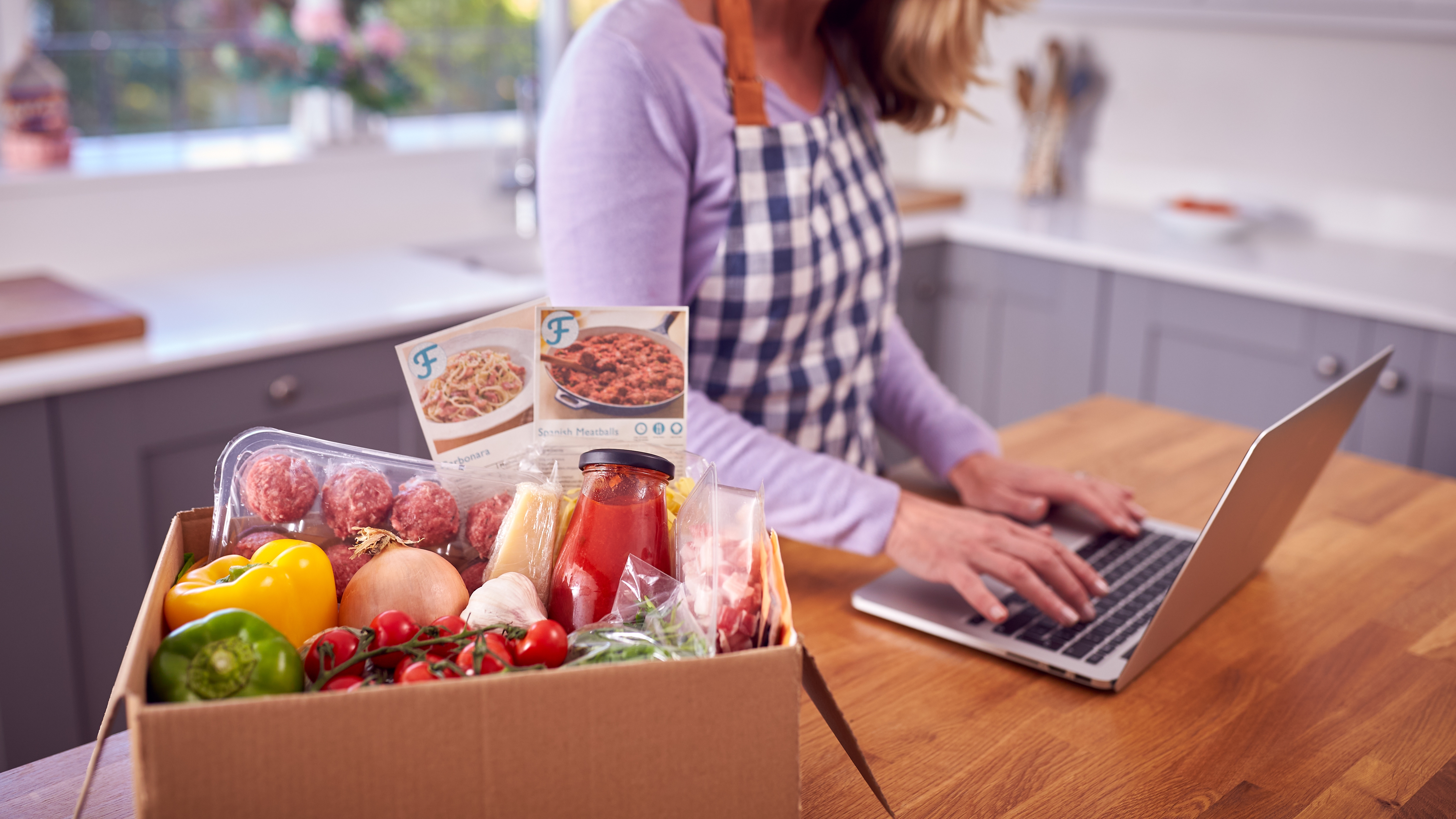 Woman wearing a purple shirt on her laptop next to a food delivery box