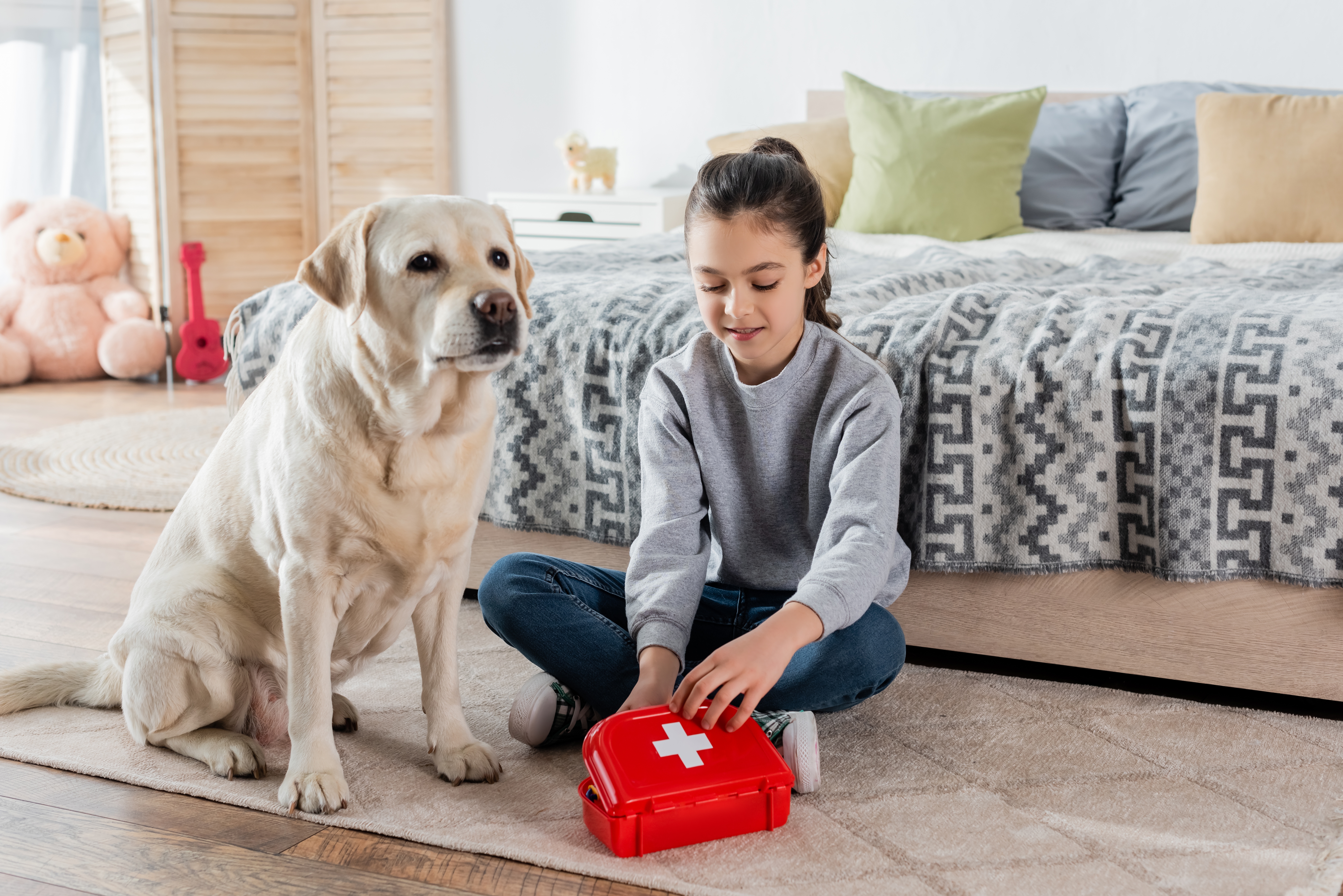 Young girl opening a first aid kit while her dog sits next to her