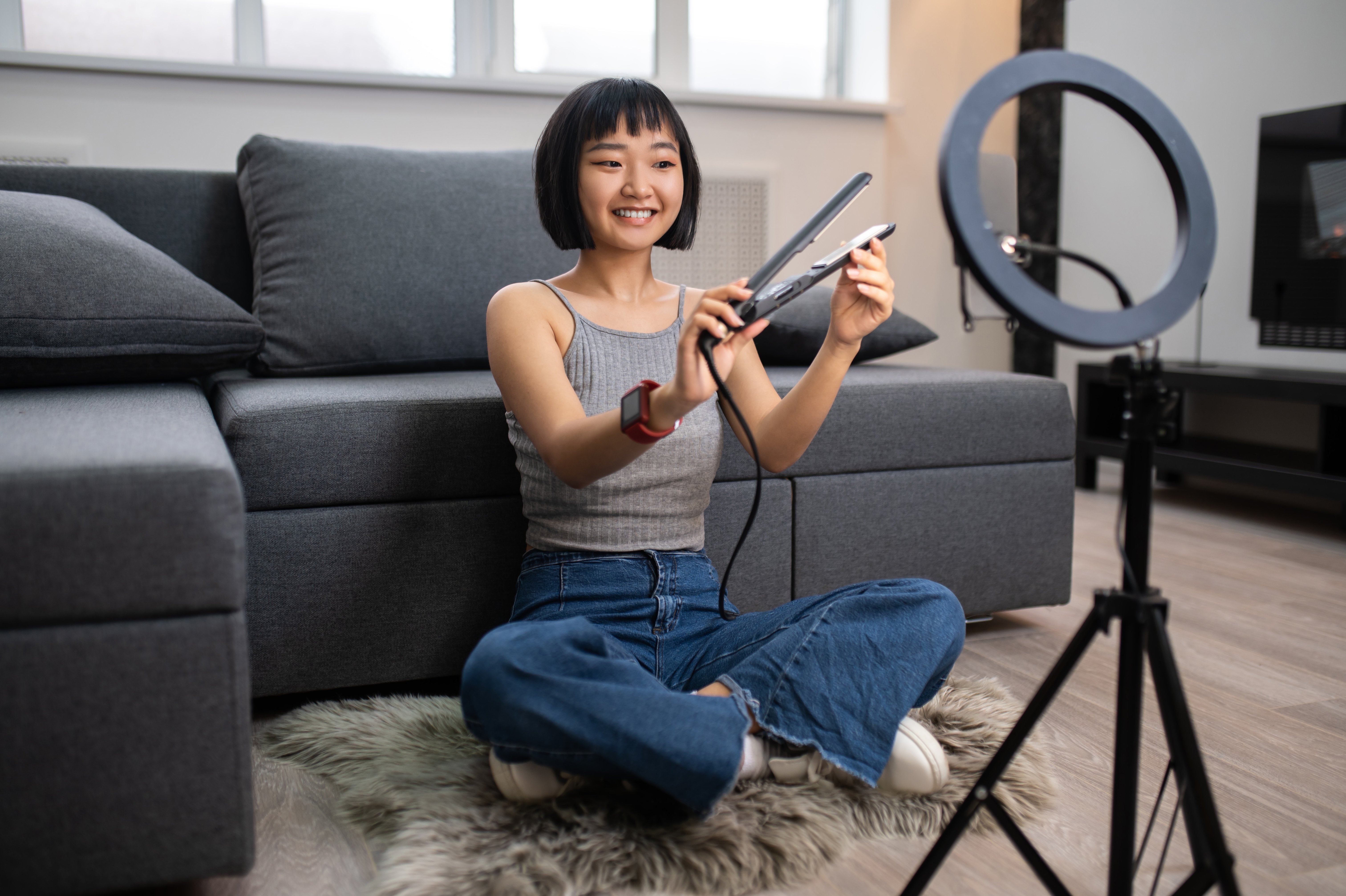 Woman sitting on the floor in front of a camera holding a curling iron