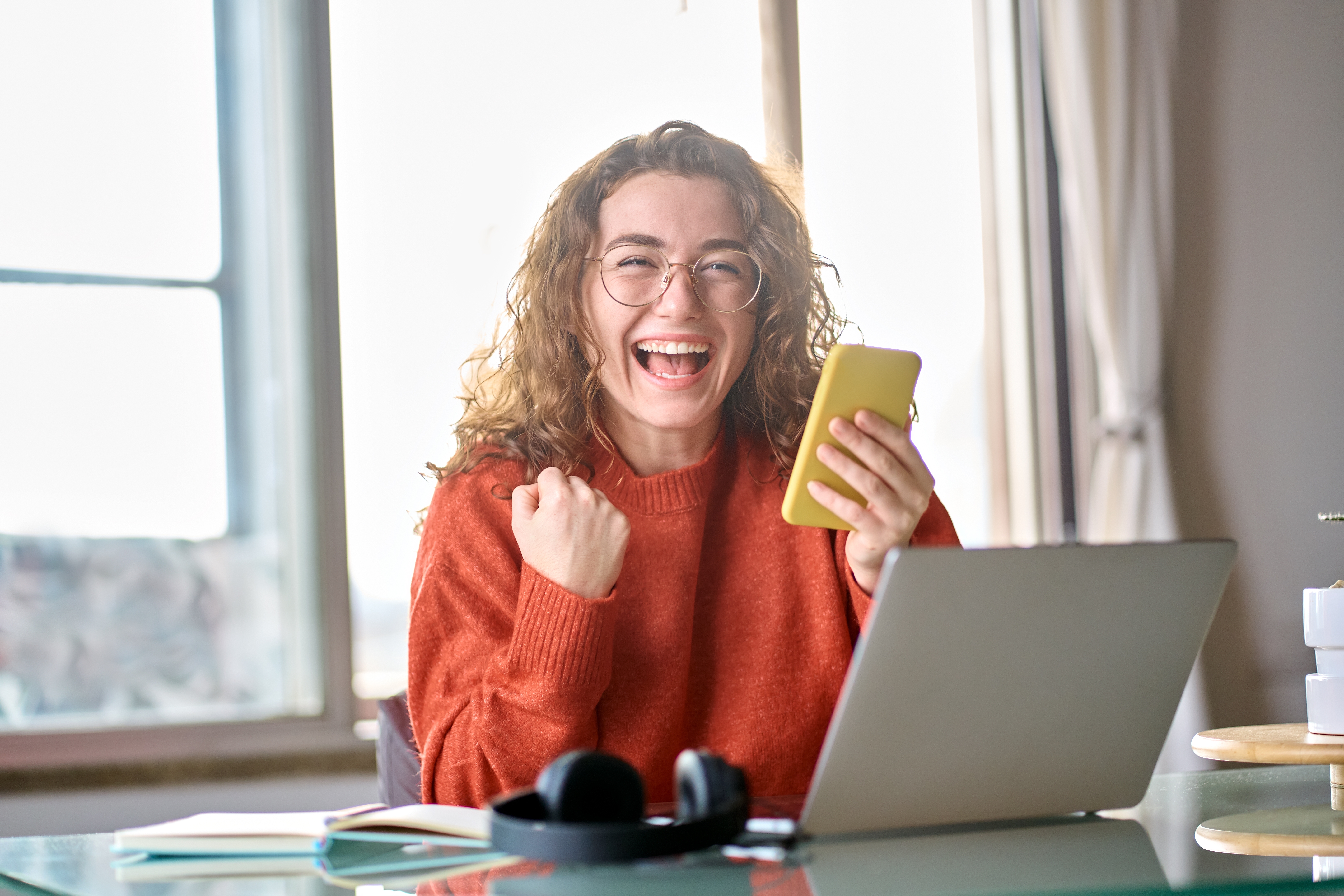 Girl wearing an orange sweater and glasses excitedly looking at her smartphone