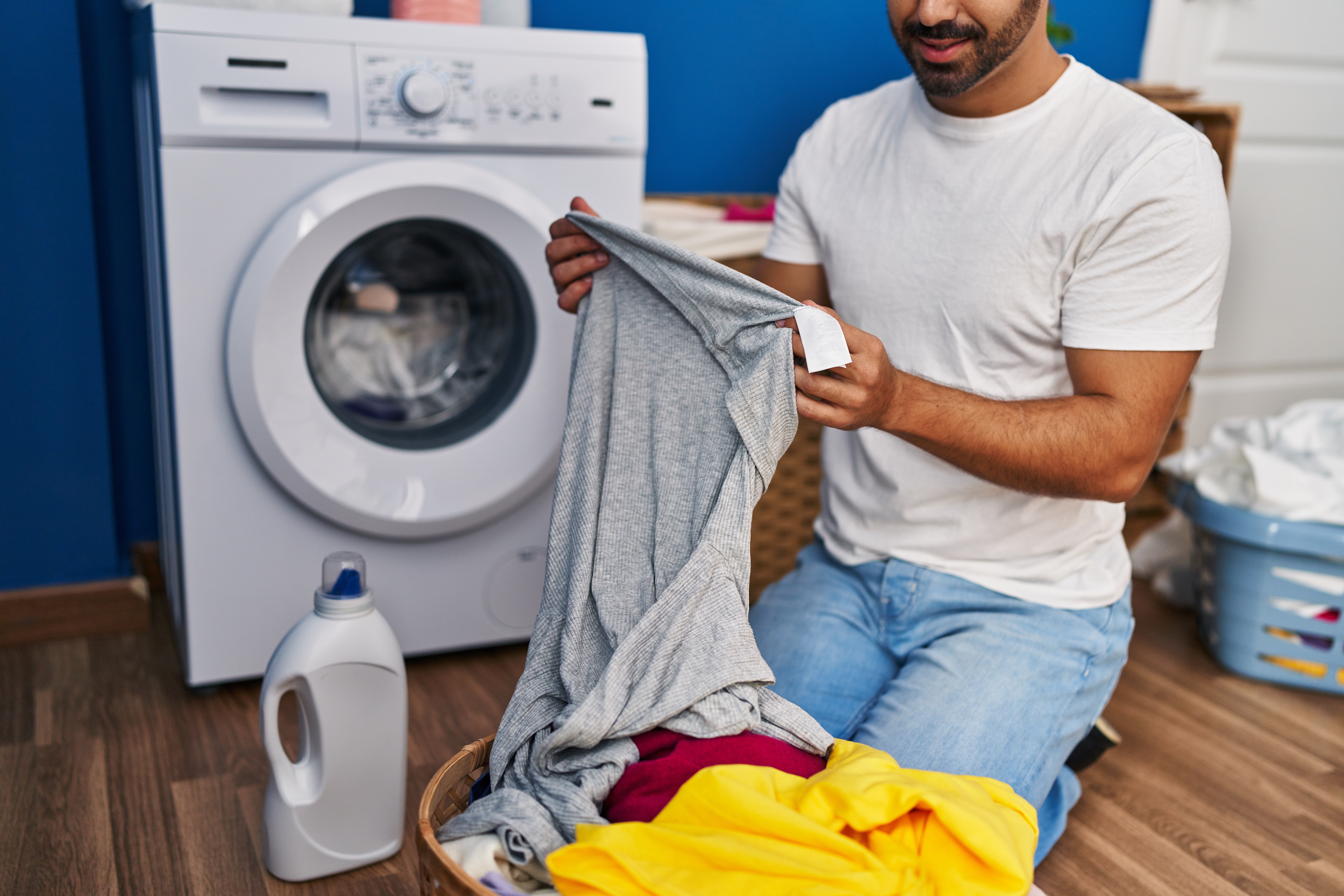 Man kneeling on the ground in front of a washing machine next to a pile of clothes