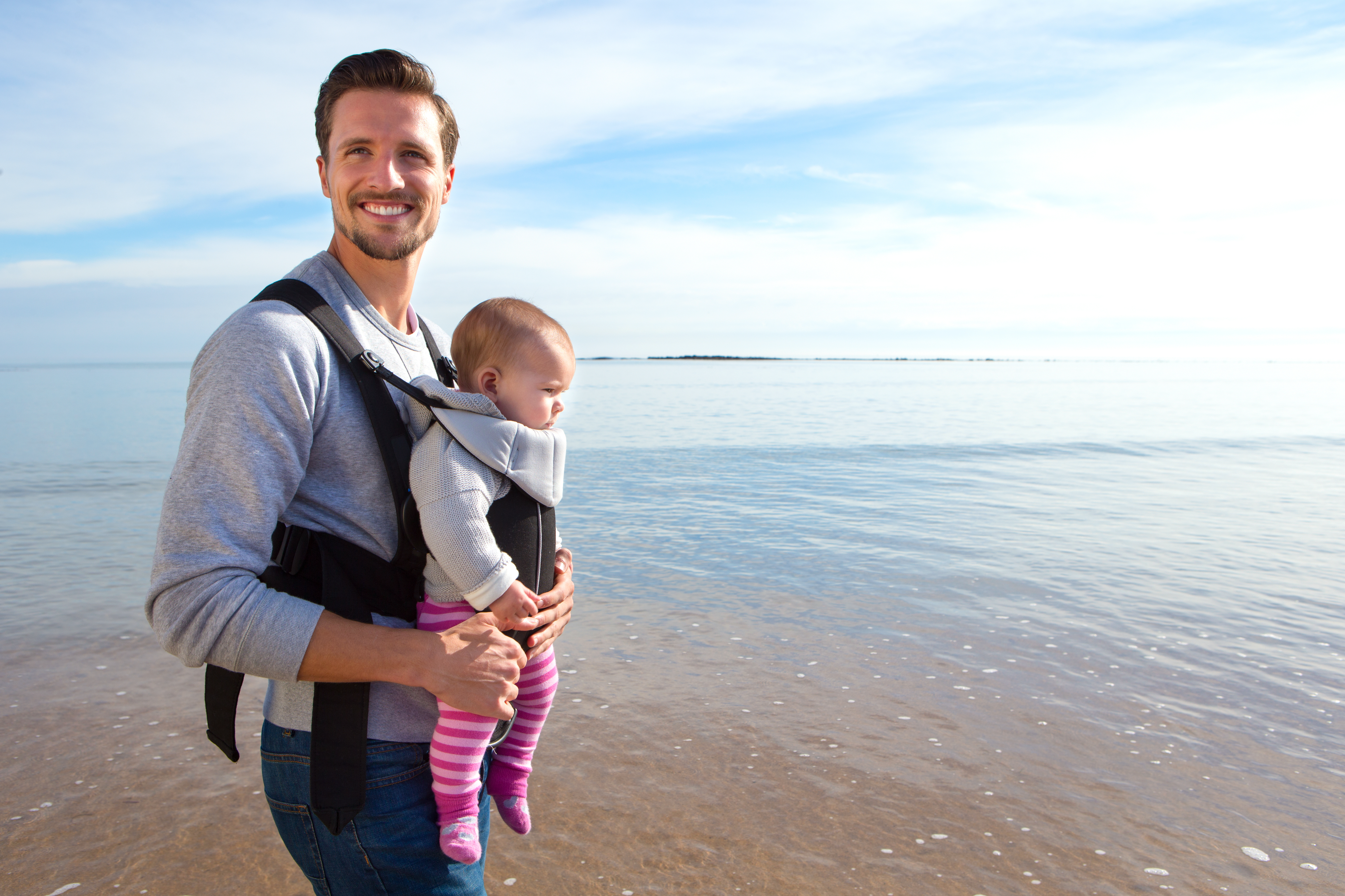 Dad at the beach holing his baby in a baby carrier