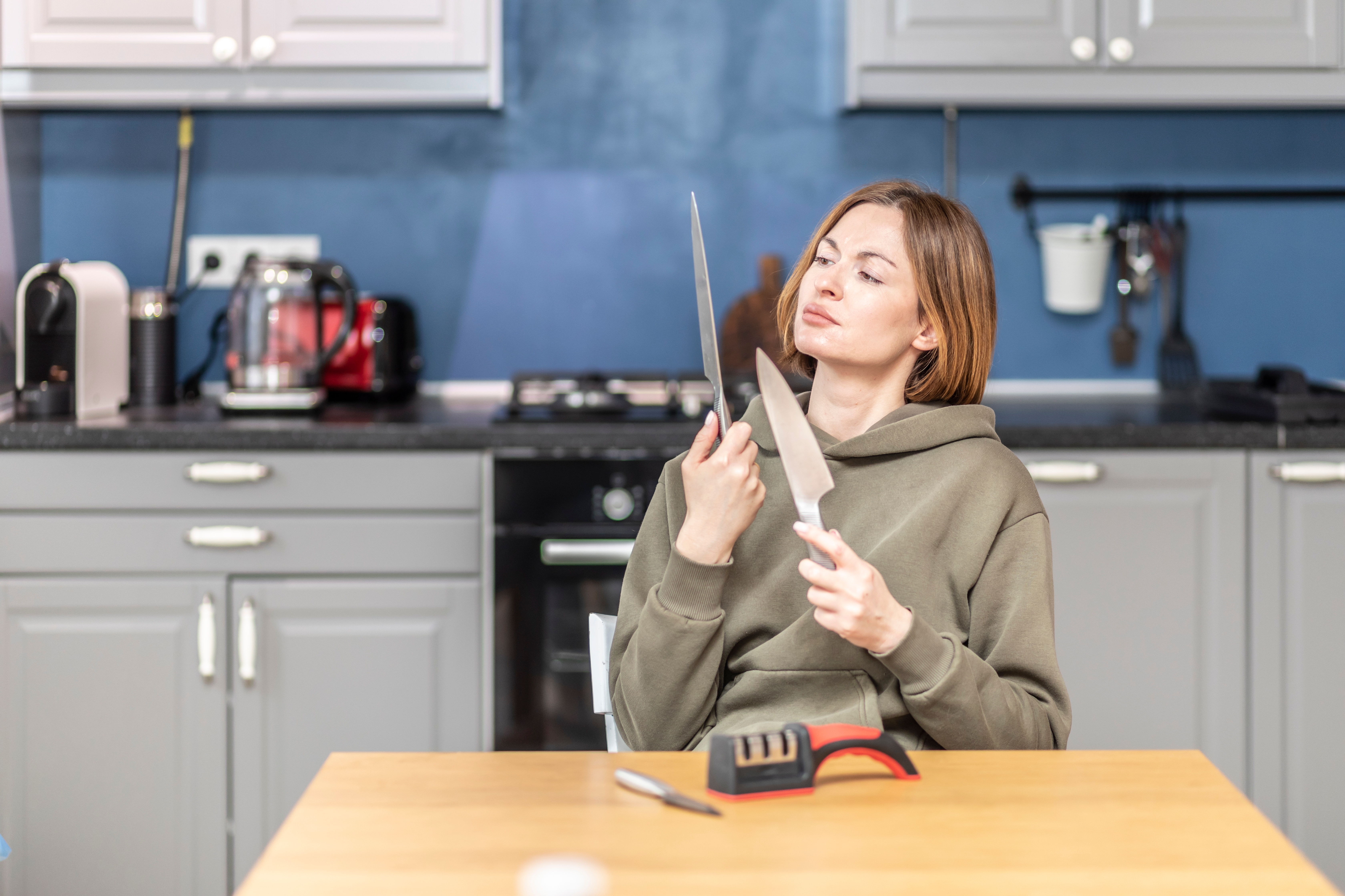 Woman sitting at table holding two kitchen knives in front of a knife sharpener