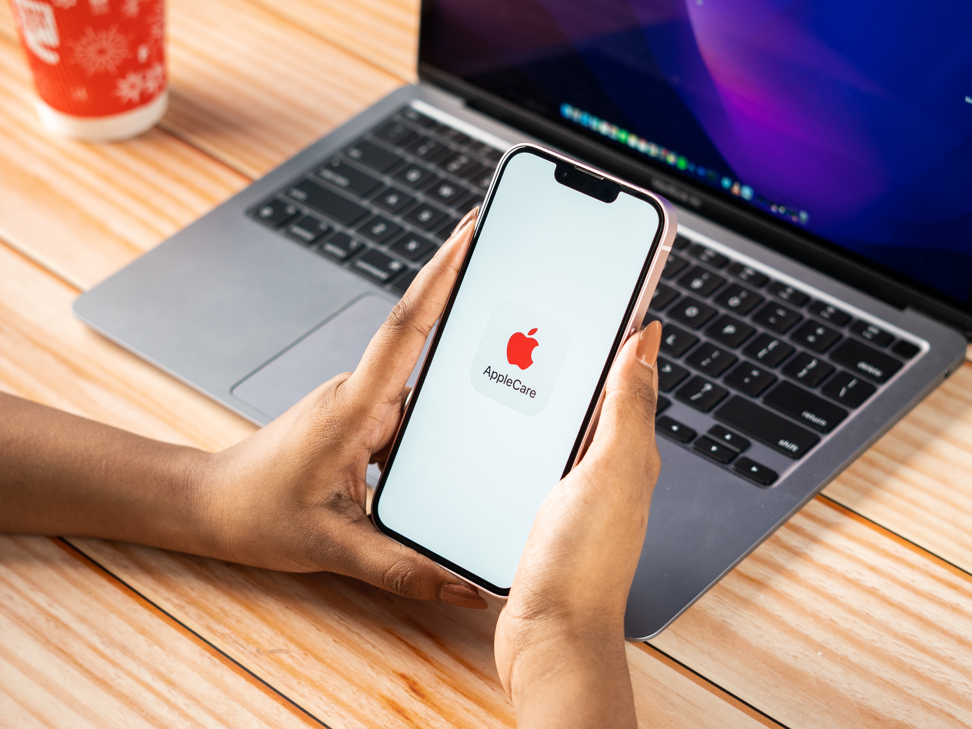 Person holding iPhone with AppleCare logo on it in front of a MacBook