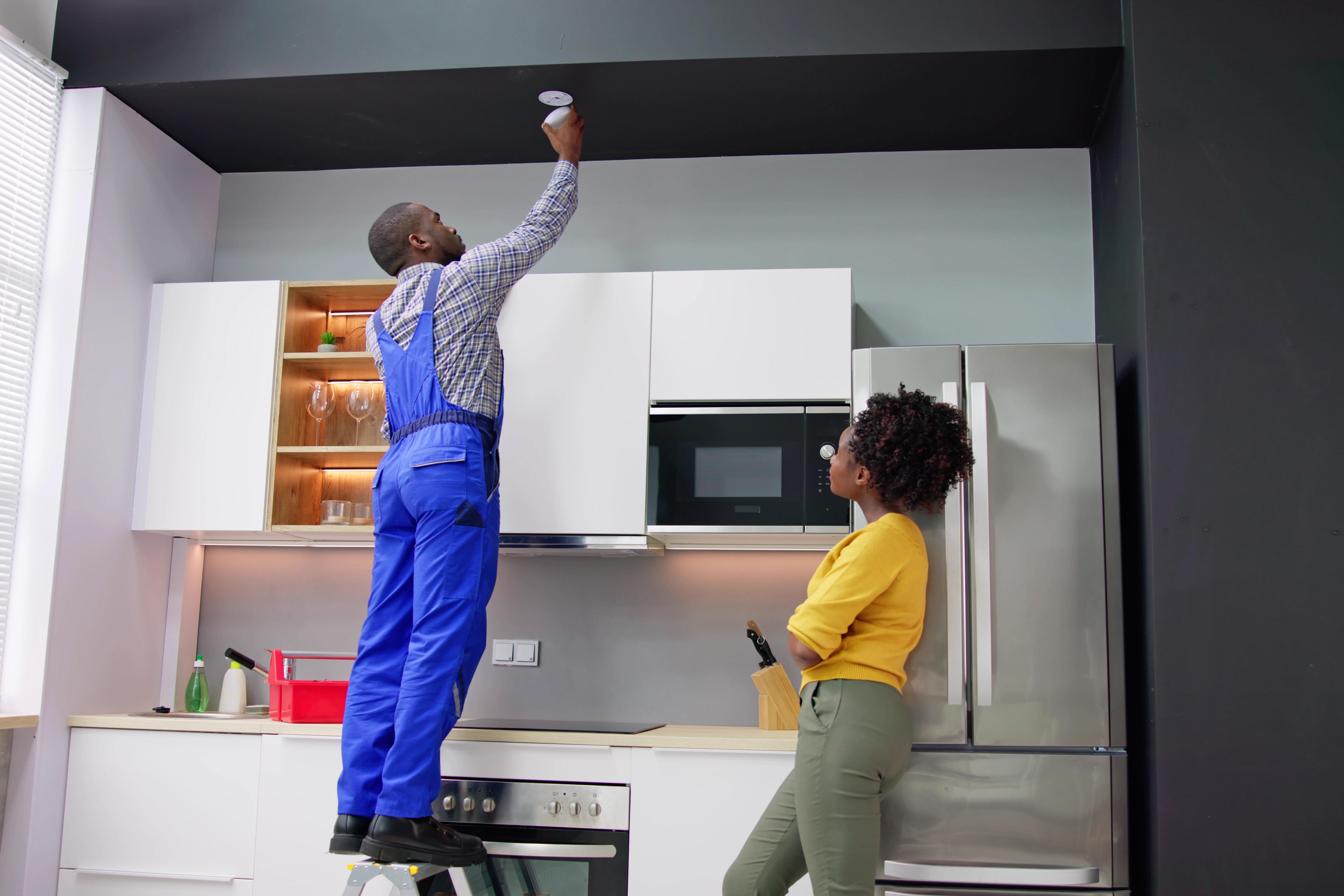 Man replacing the smoke alarm while woman stands and watches