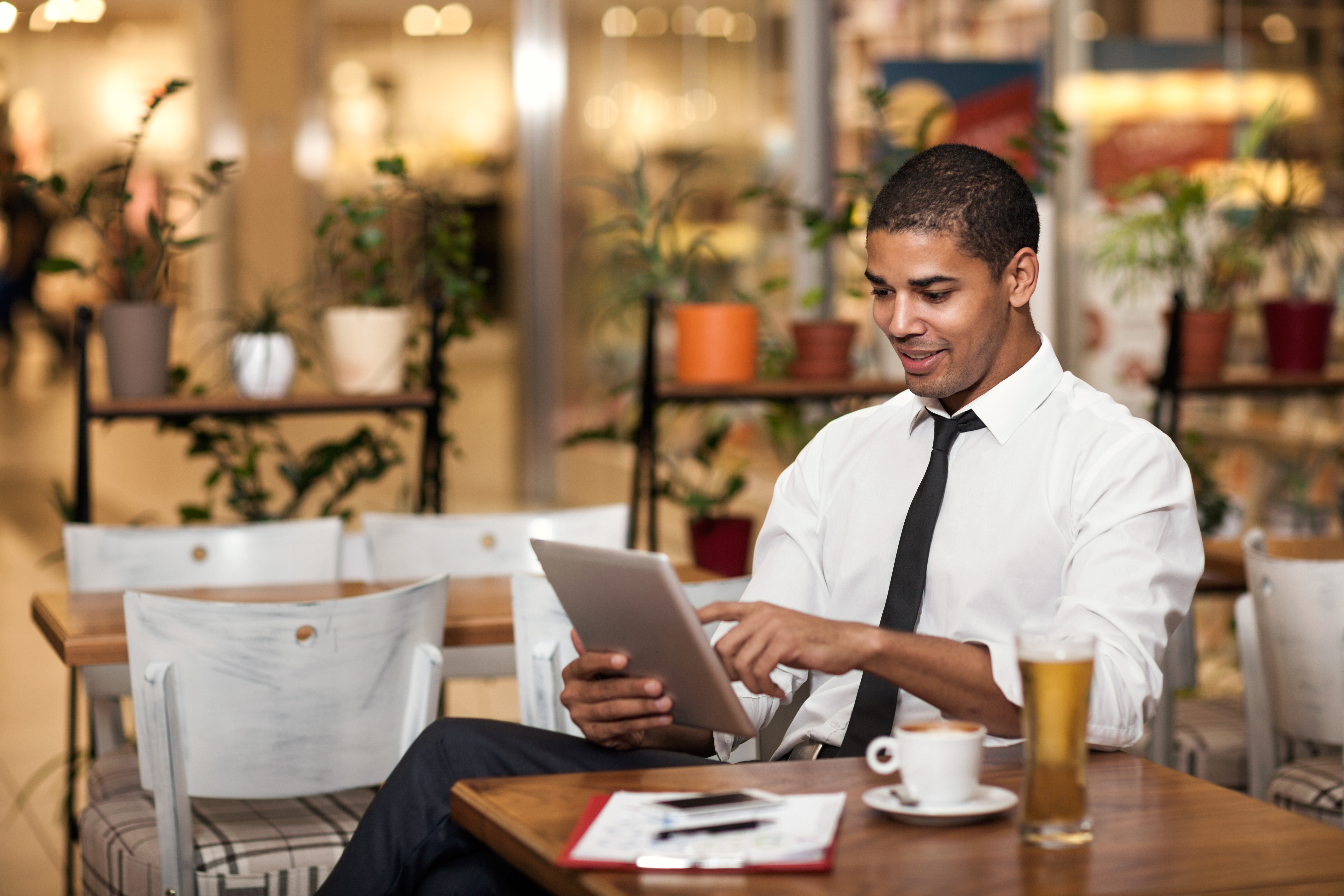 Man wearing a black tie working on a tablet in a cafe