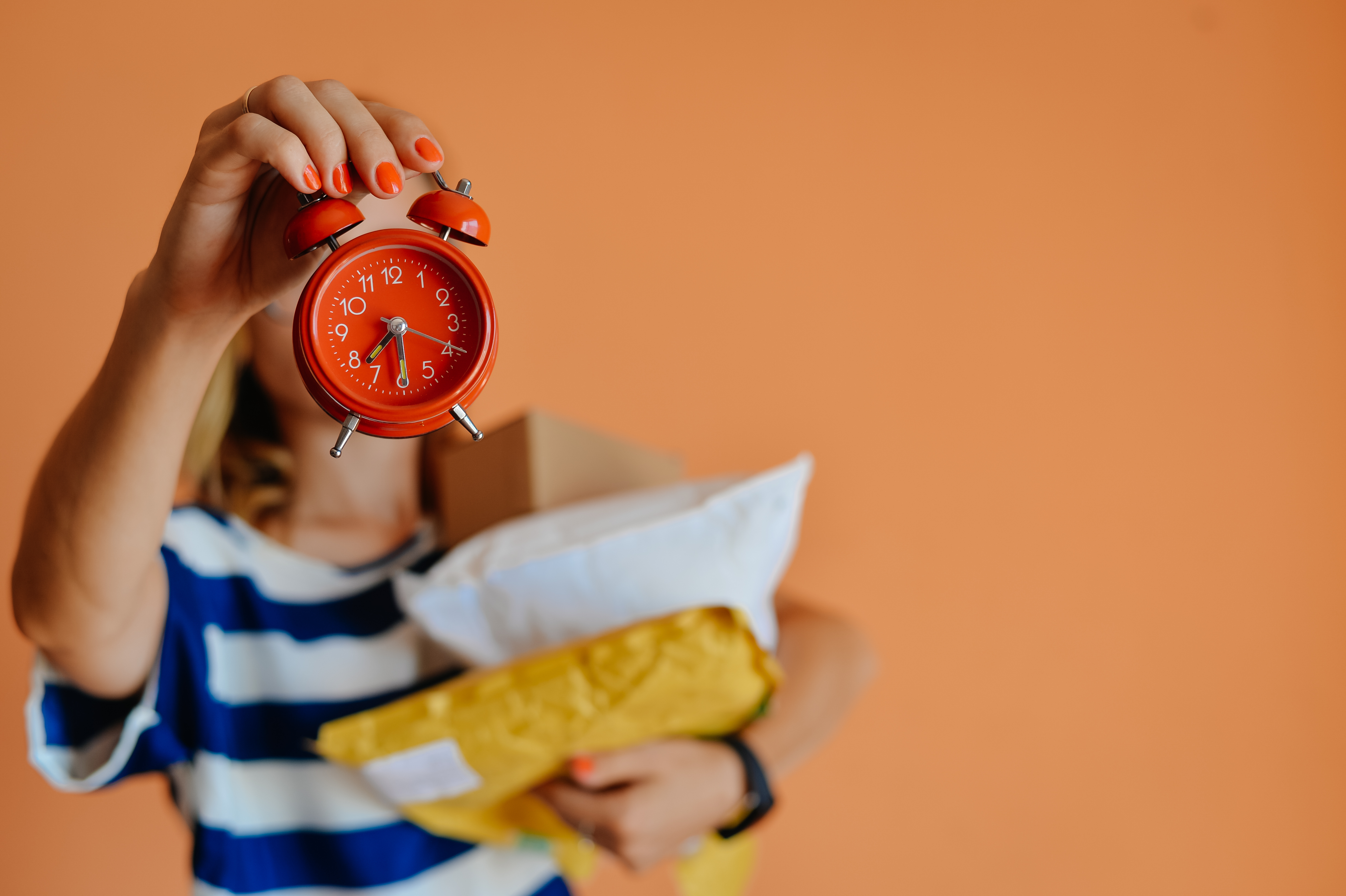 Woman with an arm full of packages holding up a red alarm clock