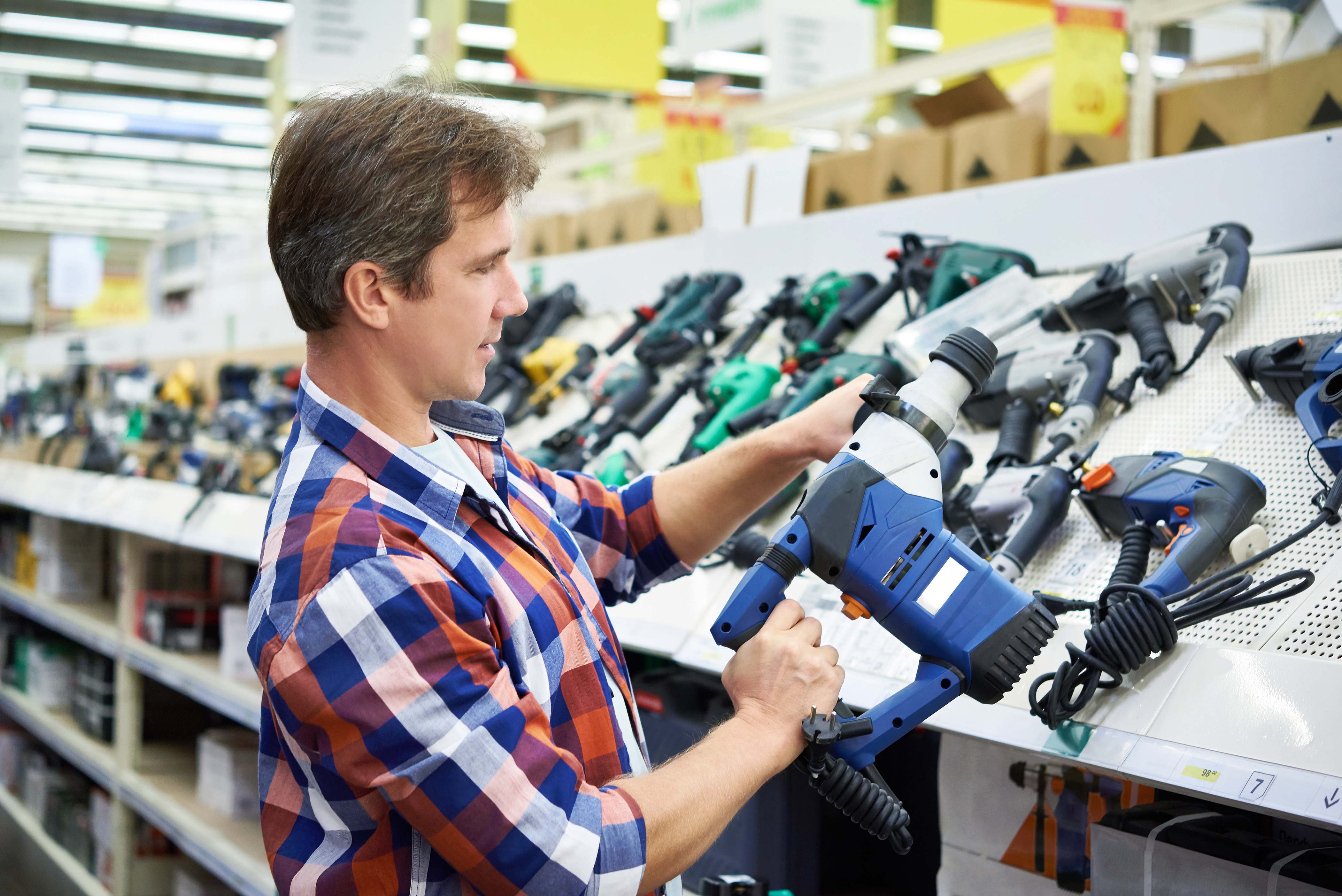 Man in a plaid shirt shopping for power tools at a home improvement store