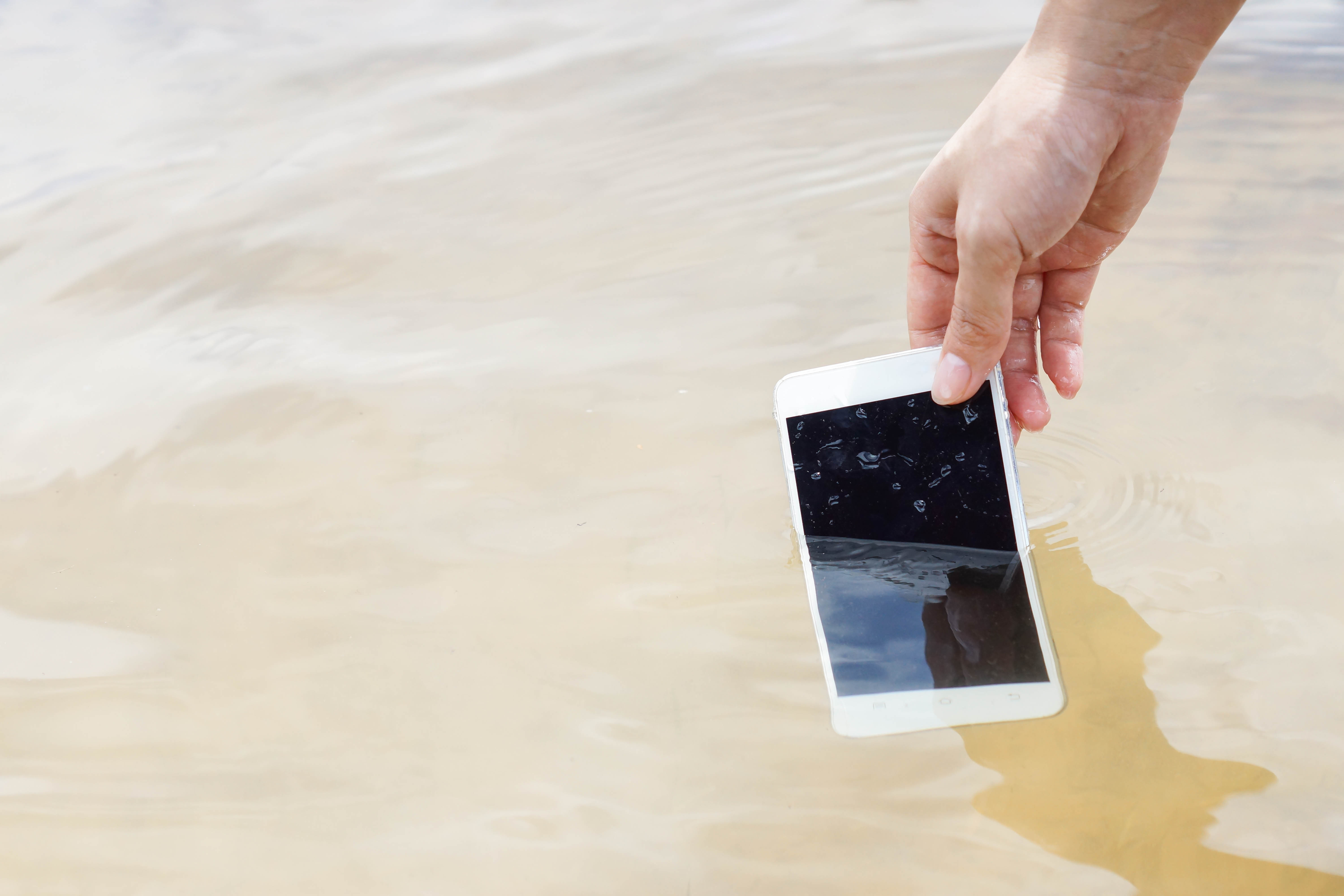 Person pulling a white smartphone out of the water