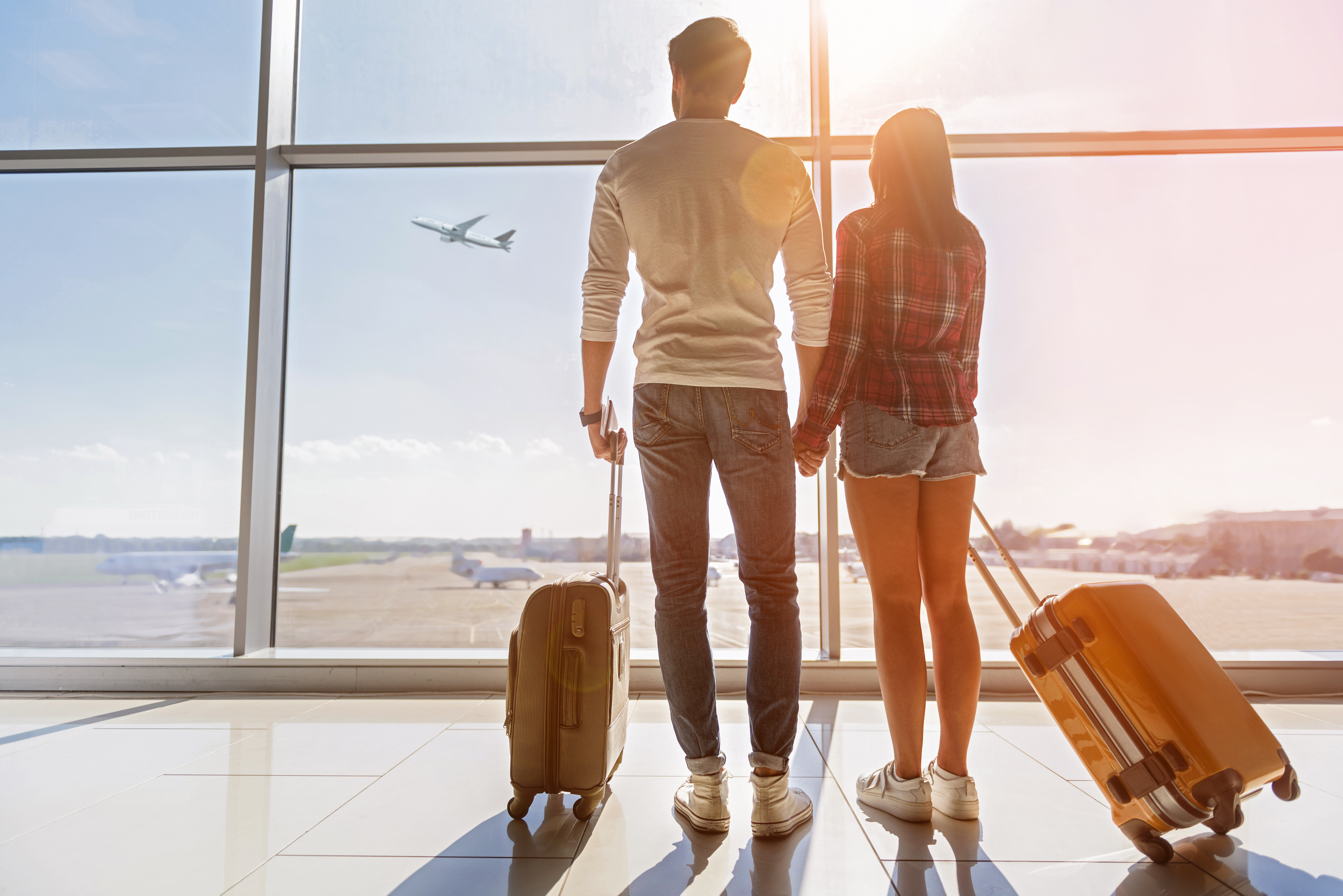 Man and woman holding hands looking out window at airport