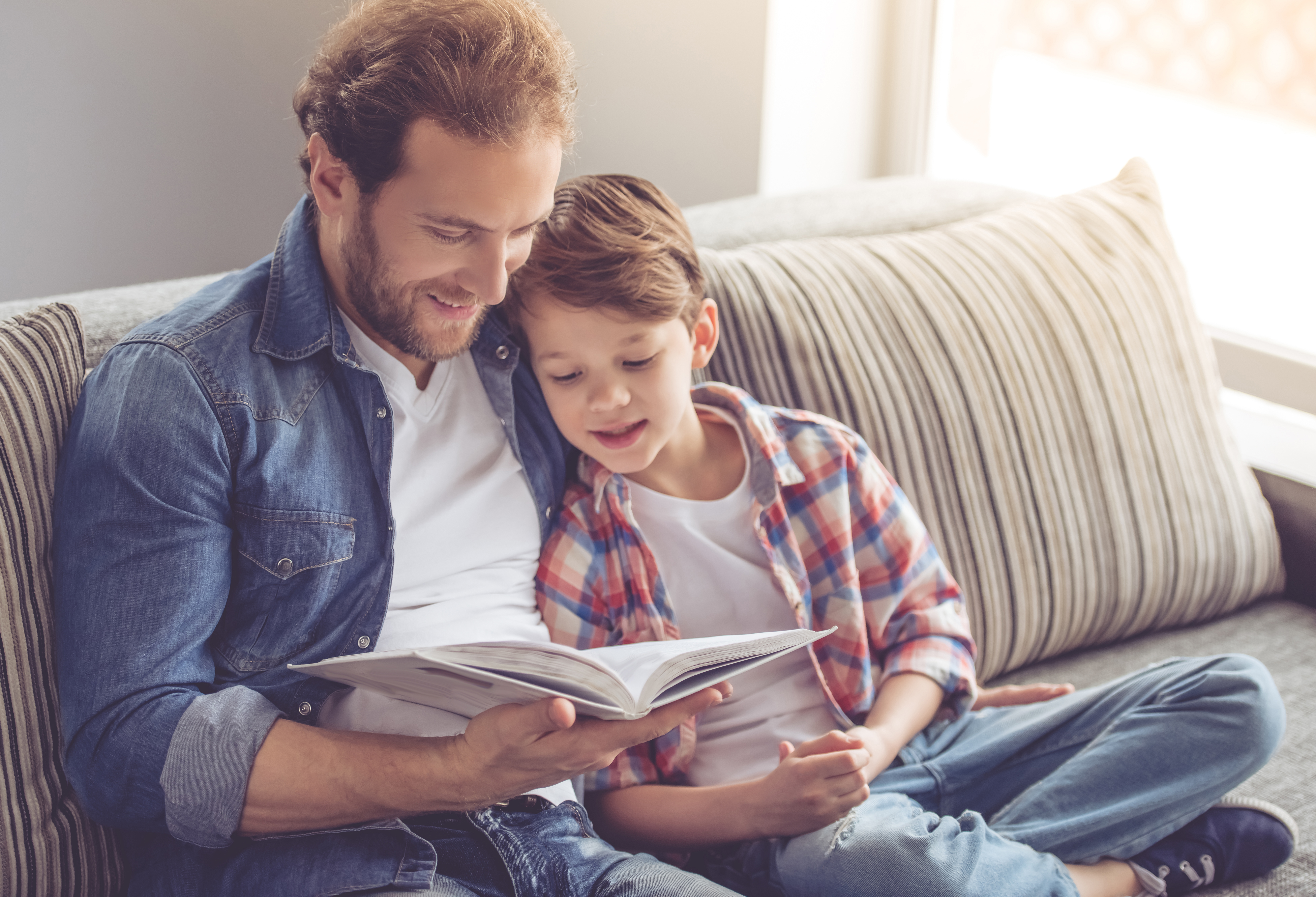 Father and son sitting on the couch reading a book together