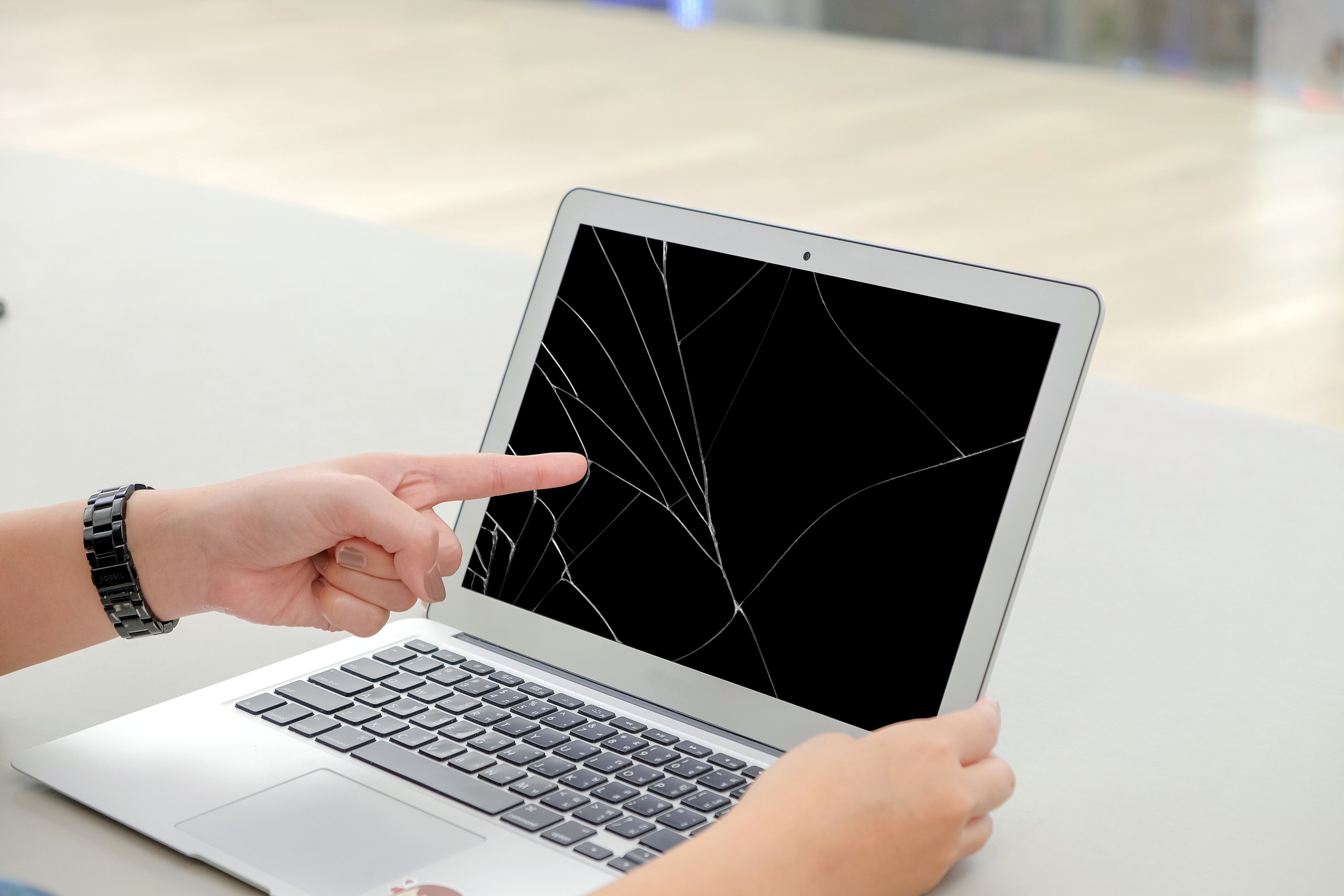 Person pointing at a cracked MacBook screen