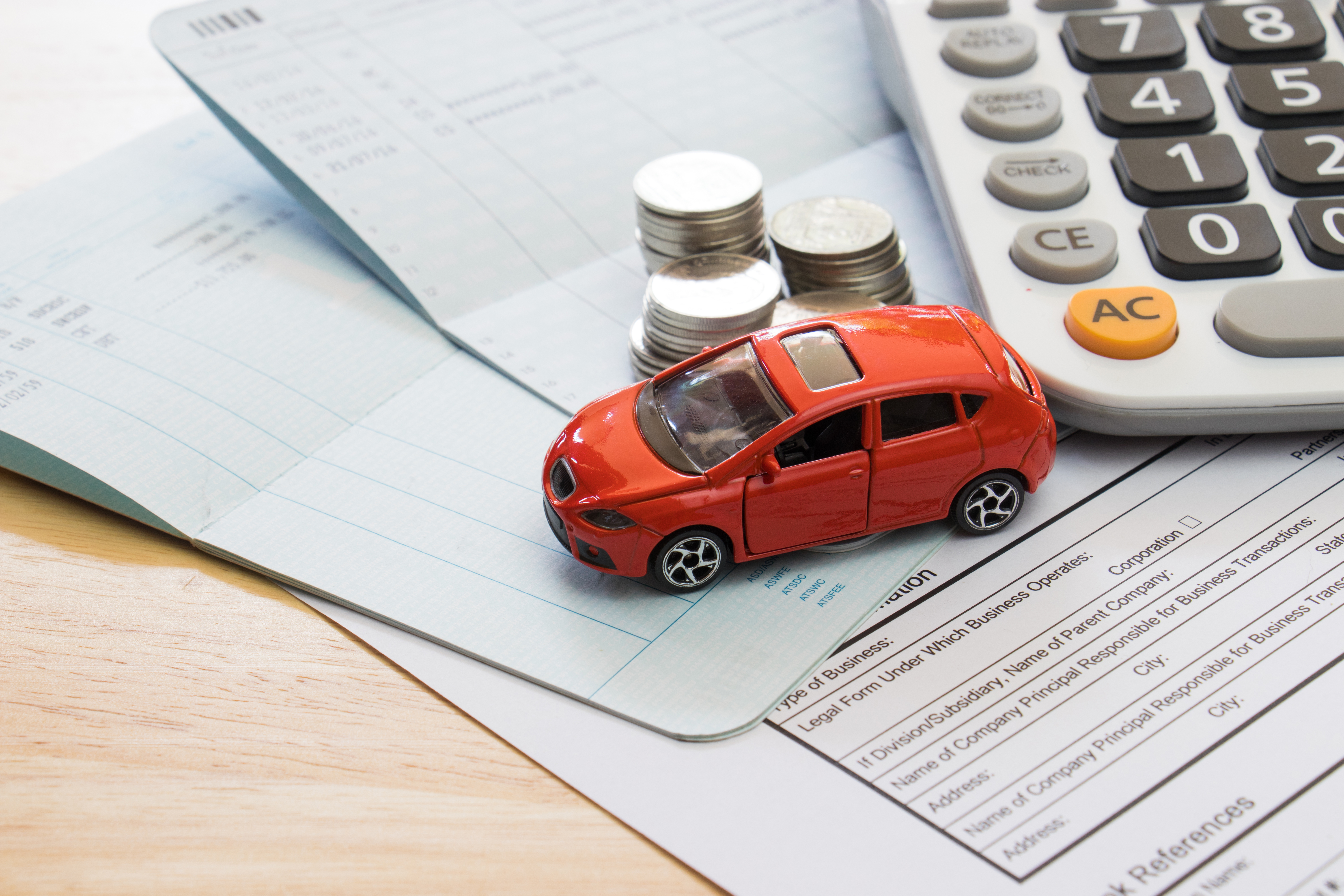 Toy car next to forms, a calculator, and a stack of coins.