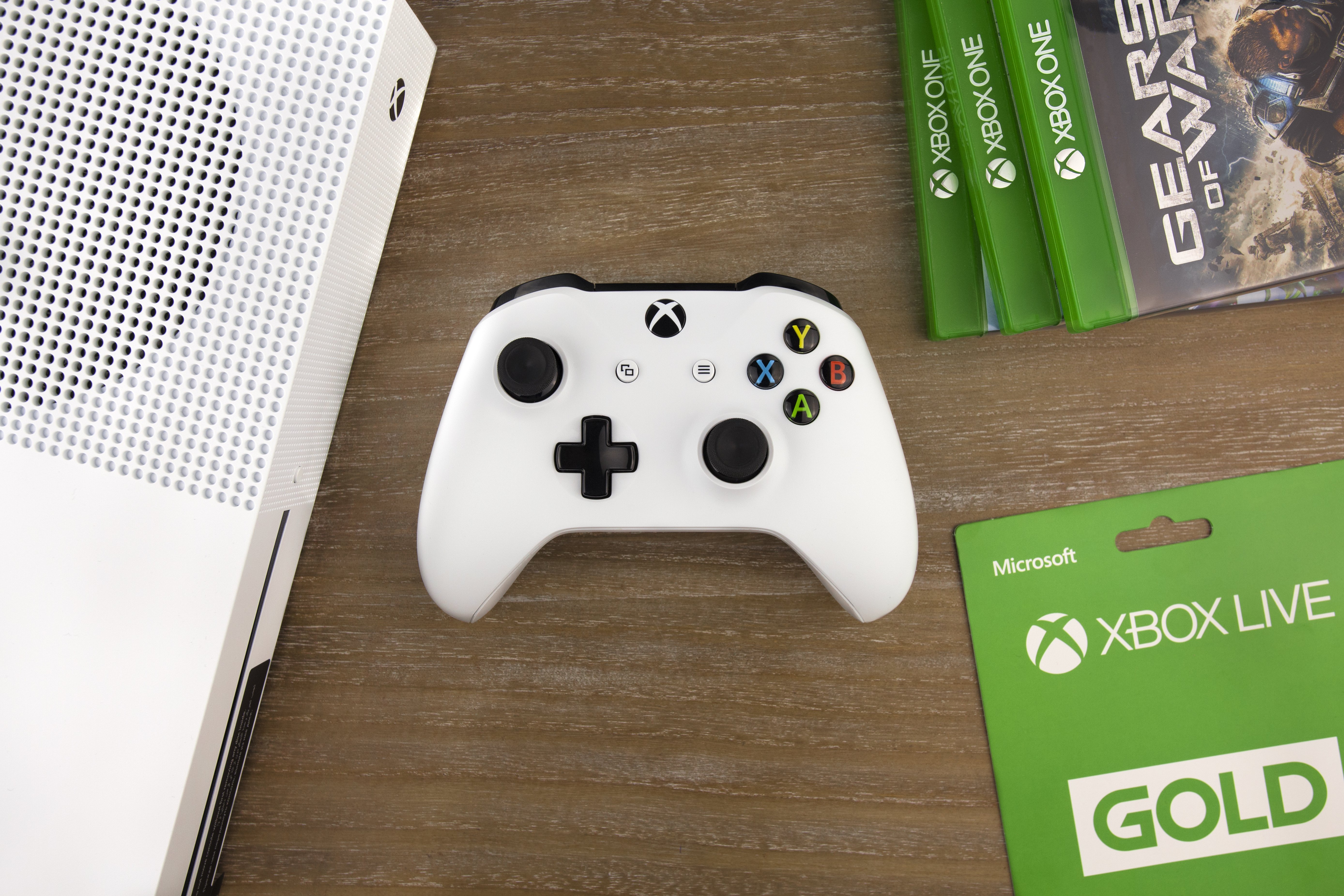 Xbox controller sitting on a desk next to an Xbox console and games