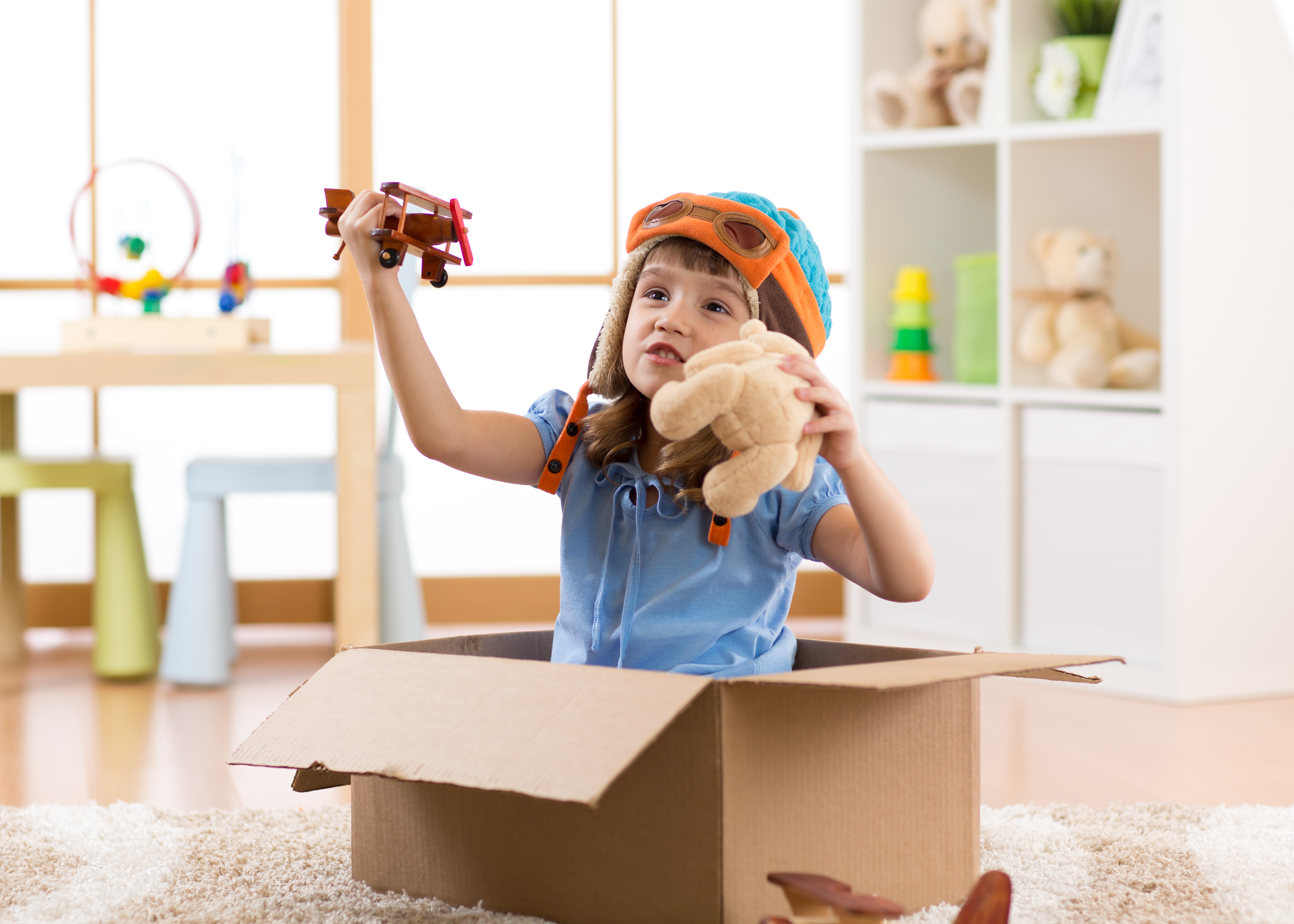 Young girl in a cardboard box playing with a stuffed animal and a toy airplane