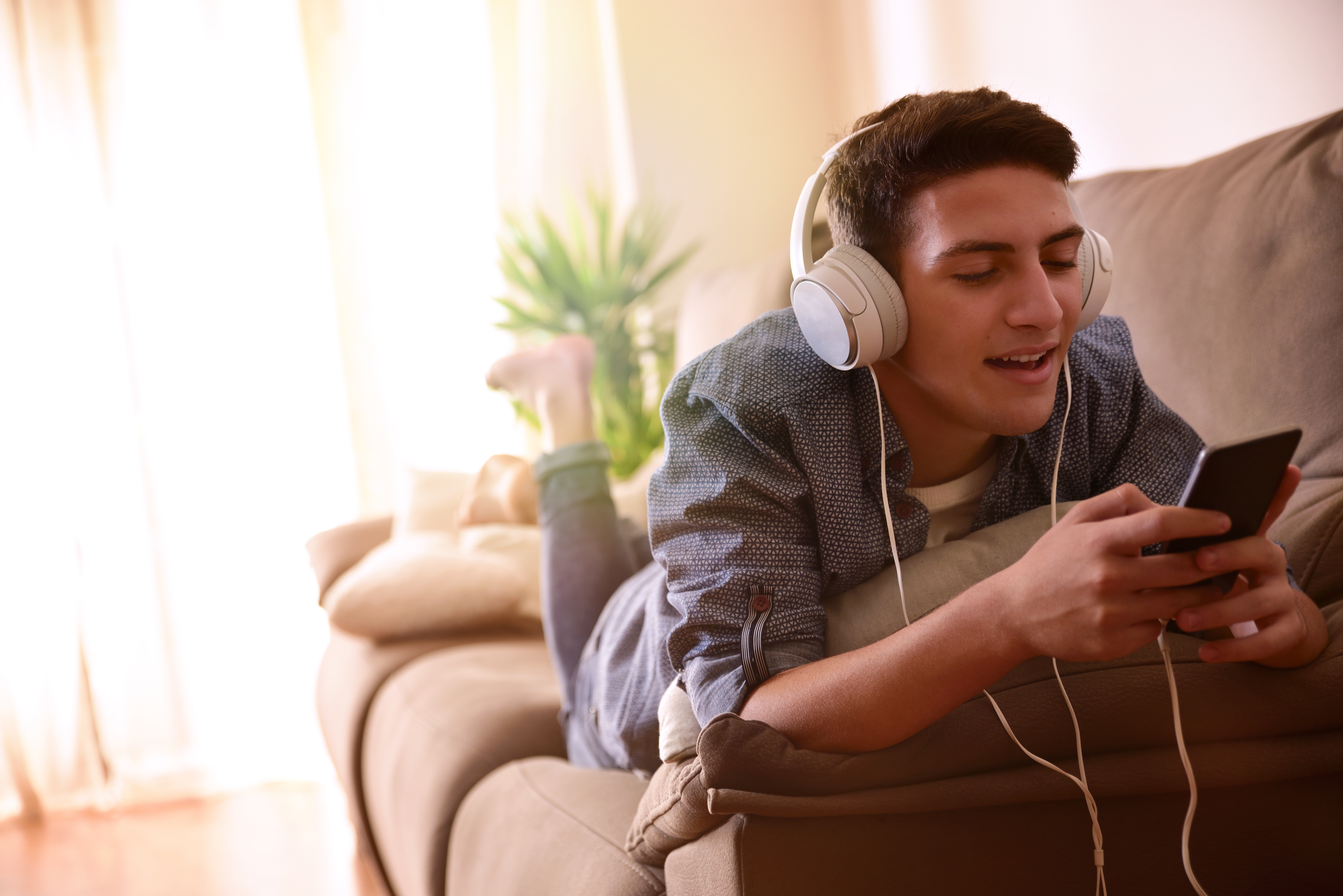 Young man with headphones on laying on the couch listening to music