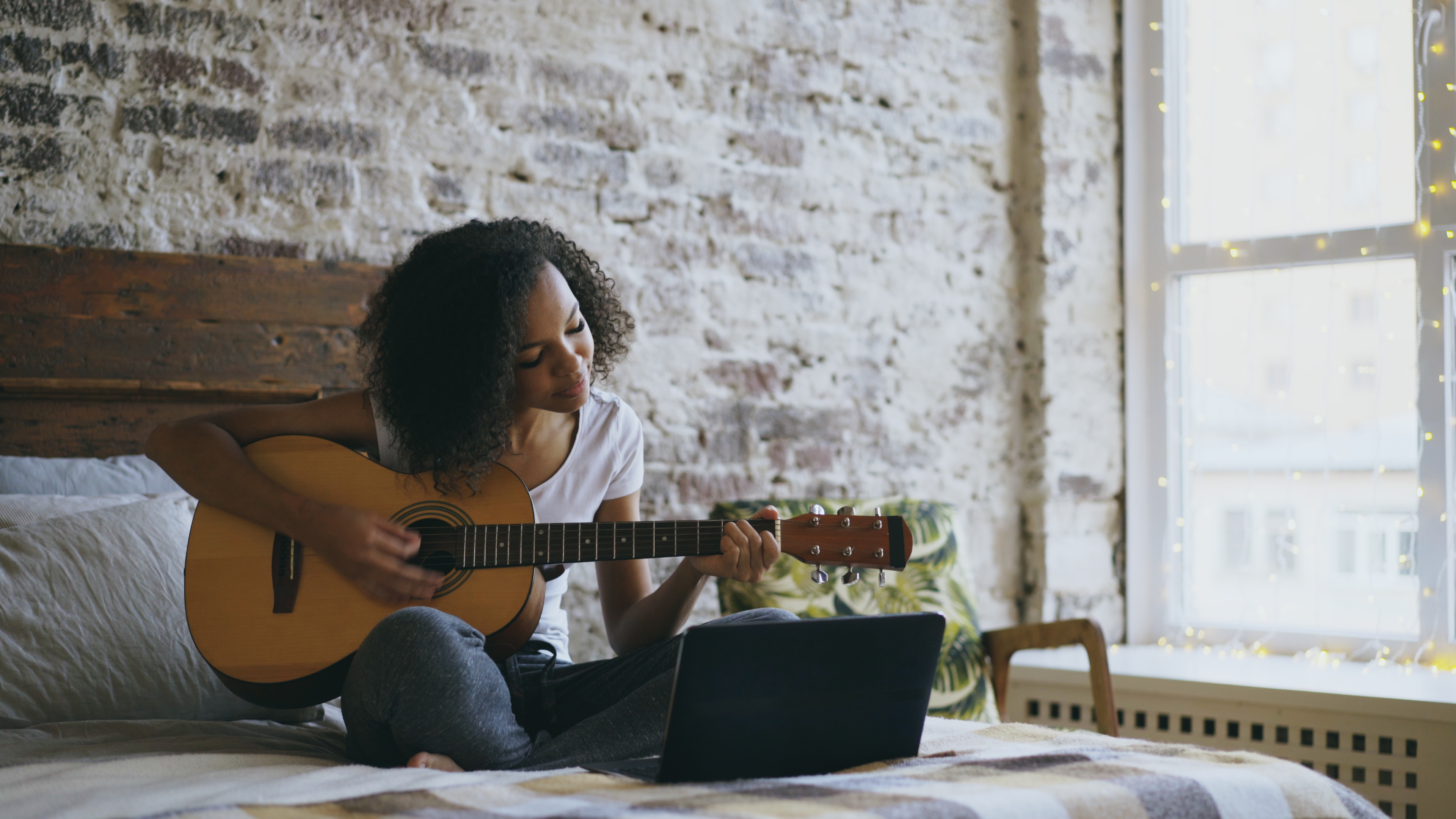 Woman sitting cross-legged on the bed playing a guitar