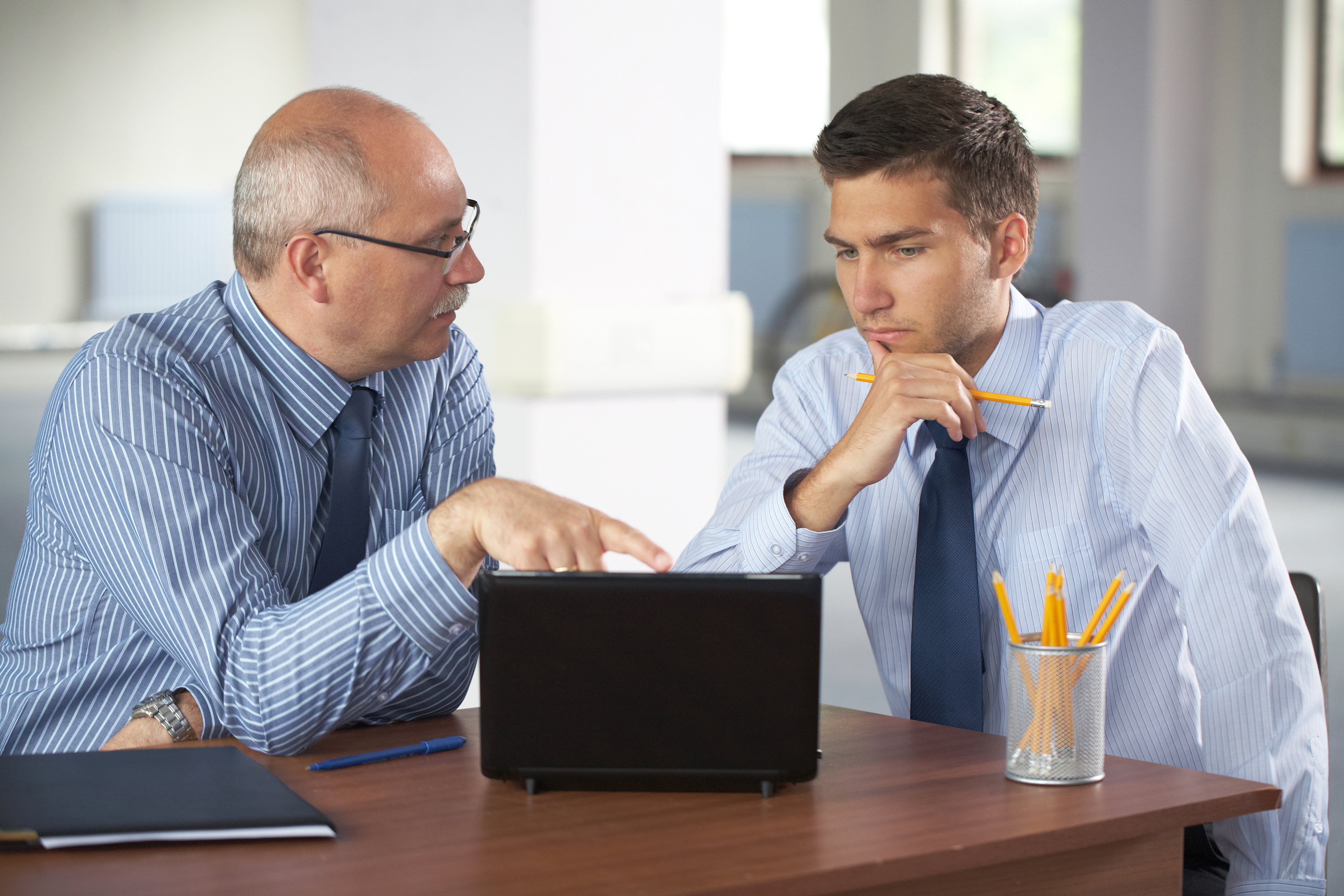Older man pointing at an open laptop talking to younger man